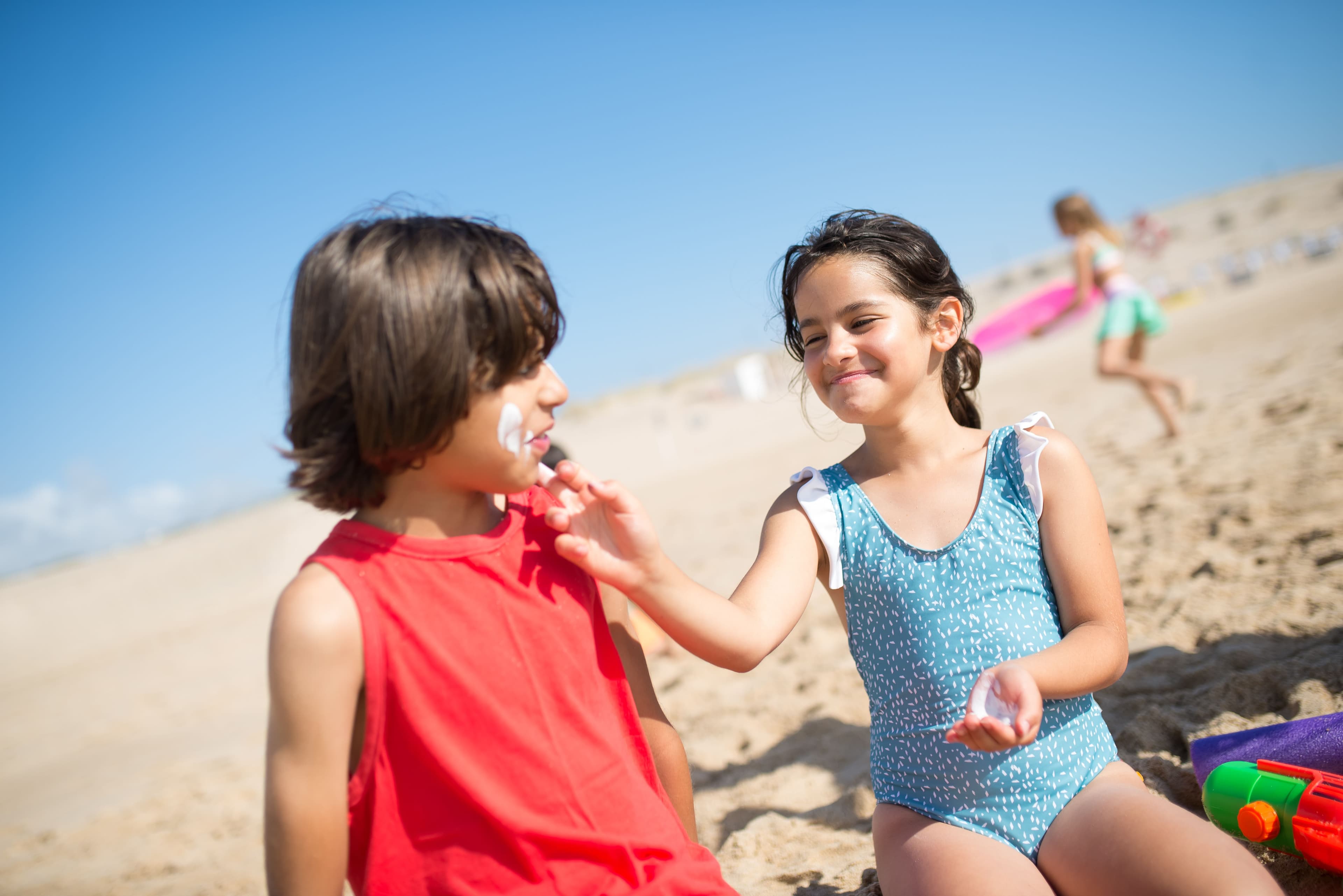 Deux enfants appliquent de la crème solaire sur une plage ensoleillée.